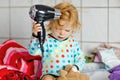 Cute little toddler girl making hairs with hair dryer. Adorable healthy baby child with wet hairs after taking bath Royalty Free Stock Photo
