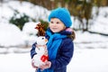 Cute little toddler girl making mini snowman and eating carrot nose. Adorable healthy happy child playing and having fun