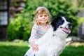 Cute little toddler girl playing with family dog in garden. Happy smiling child having fun with dog, hugging playing Royalty Free Stock Photo