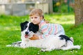 Cute little toddler girl playing with family dog in garden. Happy smiling child having fun with dog, hugging playing Royalty Free Stock Photo