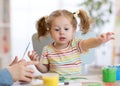 Cute little toddler girl in striped shirt and pony tails paints in the art class