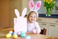 Cute little toddler girl wearing Easter bunny ears playing with colored pastel eggs. Happy baby child unpacking gifts Royalty Free Stock Photo