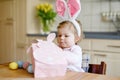 Cute little toddler girl wearing Easter bunny ears playing with colored pastel eggs. Happy baby child unpacking gifts Royalty Free Stock Photo