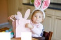 Cute little toddler girl wearing Easter bunny ears playing with colored pastel eggs. Happy baby child unpacking gifts Royalty Free Stock Photo