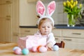 Cute little toddler girl wearing Easter bunny ears playing with colored pastel eggs. Happy baby child unpacking gifts Royalty Free Stock Photo