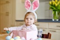 Cute little toddler girl wearing Easter bunny ears playing with colored pastel eggs. Happy baby child unpacking gifts Royalty Free Stock Photo