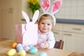 Cute little toddler girl wearing Easter bunny ears playing with colored pastel eggs. Happy baby child unpacking gifts Royalty Free Stock Photo