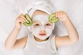 Cute little two three years old girl with a towel over her wet hair, facial mask on her face, relaxed and lying on white Royalty Free Stock Photo