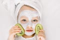 Cute little two three years old girl with a towel over her wet hair, facial mask on her face, relaxed and lying on white Royalty Free Stock Photo