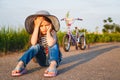 Cute little unhappy girl in big sun hat sitting on road with her bicycle behind her