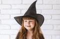 Cute Little Witch In A black Hat Against A white brick wall.Portrait of a 4-year-old girl at the Halloween festival.A pretty Royalty Free Stock Photo