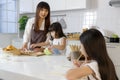 A cute little 7 years old Asian girl sitting and doing homework in kitchen while her mother teaching her younger sister how to Royalty Free Stock Photo