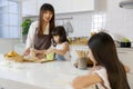 A cute little 7 years old Asian girl sitting and doing homework in kitchen while her mother teaching her younger sister how to Royalty Free Stock Photo