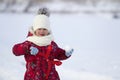 Cute little young funny toothless child girl in warm clothing playing having fun making snowballs on winter cold day on white brig