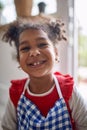 Cute little young girl child standing in a kitchen waring a blue chekered apron and feeling joyful, smiling Royalty Free Stock Photo