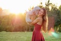 Cute long-haired tanned woman enigmatic smile in a red dress tosses throws a gray teddy bear toy in hands in the park