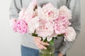 Cute and lovely peony flowers in women`s hands.. many layered petals. Bunch pale pink peonies flowers light gray