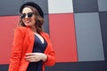 Cute lovely young woman in sunglasses, red jacket, fashion hat, standing over abstract background outdoor. Portrait fashion model Royalty Free Stock Photo