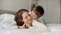 Cute loving boy in pajamas lying with mother in bed and kissing her. Concept of family happiness, relaxing at home, having fun in Royalty Free Stock Photo