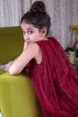 Cute lovlely middle eastern girl with dark red dress and collected hair posing and liying on green sofa at home interior.