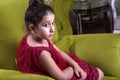 Cute lovlely middle eastern girl with dark red dress and collected hair posing and liying on green sofa at home interior.