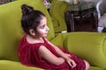 Cute lovlely middle eastern girl with dark red dress and collected hair posing and liying on green sofa at home interior.