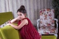 Cute lovlely middle eastern girl with dark red dress and collected hair posing and liying on green sofa at home interior.