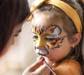 Cute makeup little tiger. girl getting face painting outdoors,