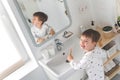 Cute male kid in pajamas cleaning teeth with eco friendly toothbrush comfortable minimalist bathroom