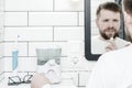 Cute man cleans his teeth with the help of electric oral irrigator with a jet of water, looking in the mirror. Copy Royalty Free Stock Photo