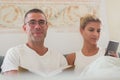 Cute man and woman in pajamas sitting on bed in early morning