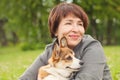 Cute mature woman cuddling puppy dog pet in summer park