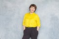 Cute mature woman portrait. Smart business lady wearing yellow shirt on gray background