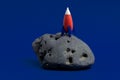 Cute miniature rocket on a moon stone on a dark blue background. Minimal space day card