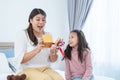 Cute mixed race child daughter, Caucasian and Asian, giving gift box to young mother for mother's day or birthday at home.