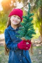 Cute Mixed Race Young Girl Wearing Red Knit Cap and Mittens Holding Mini Christmas Tree Royalty Free Stock Photo