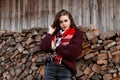 Cute model of a rural young woman in a stylish knitted sweater with a fashionable scarf stands near an old wooden wall with logs. Royalty Free Stock Photo