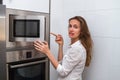 Cute modern woman in the kitchen opening the microwave and disappointed in the result of cooking. Royalty Free Stock Photo