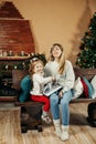 Cute mom and daughter are looking through a family photo album on Christmas Eve, spending time together by the fireplace Royalty Free Stock Photo