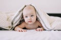 Portrait of baby hiding under the white blanket. Cute 8 month baby girl crawling in bed. Tummy Time. Textile and bedding for kids Royalty Free Stock Photo