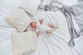 Cute baby in a white bodysuit and socks, lying on his back on bed Royalty Free Stock Photo