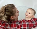 A cute mother is bathing a baby boy in clear water in a bathtub