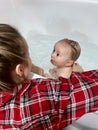 A cute mother is bathing a baby boy in clear water in a bathtub