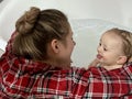 A cute mother is bathing a baby boy in clear water in a bathtub