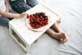Cute mother and her daughter are sitting on the bed and eating strawberries and cherries. Plate with berries and legs of