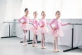 cute multiethnic kids in pink tutu skirts exercising and smiling at camera