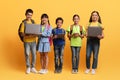 Cute multiethnic schoolers children with various gadgets on yellow background