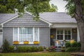 Cute and neat cottage house with grey painted bricks and wooden shindles with wicker chairs on porch and bright yellow window Royalty Free Stock Photo