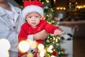 Cute newborn baby boy next to a Christmas tree with festive decoration and ferry lights for New Year celebration