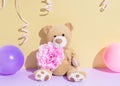 Cute newborn baby girl card. Teddy bear with festive decoration on the gold and purple background. Baby shower, birthday,